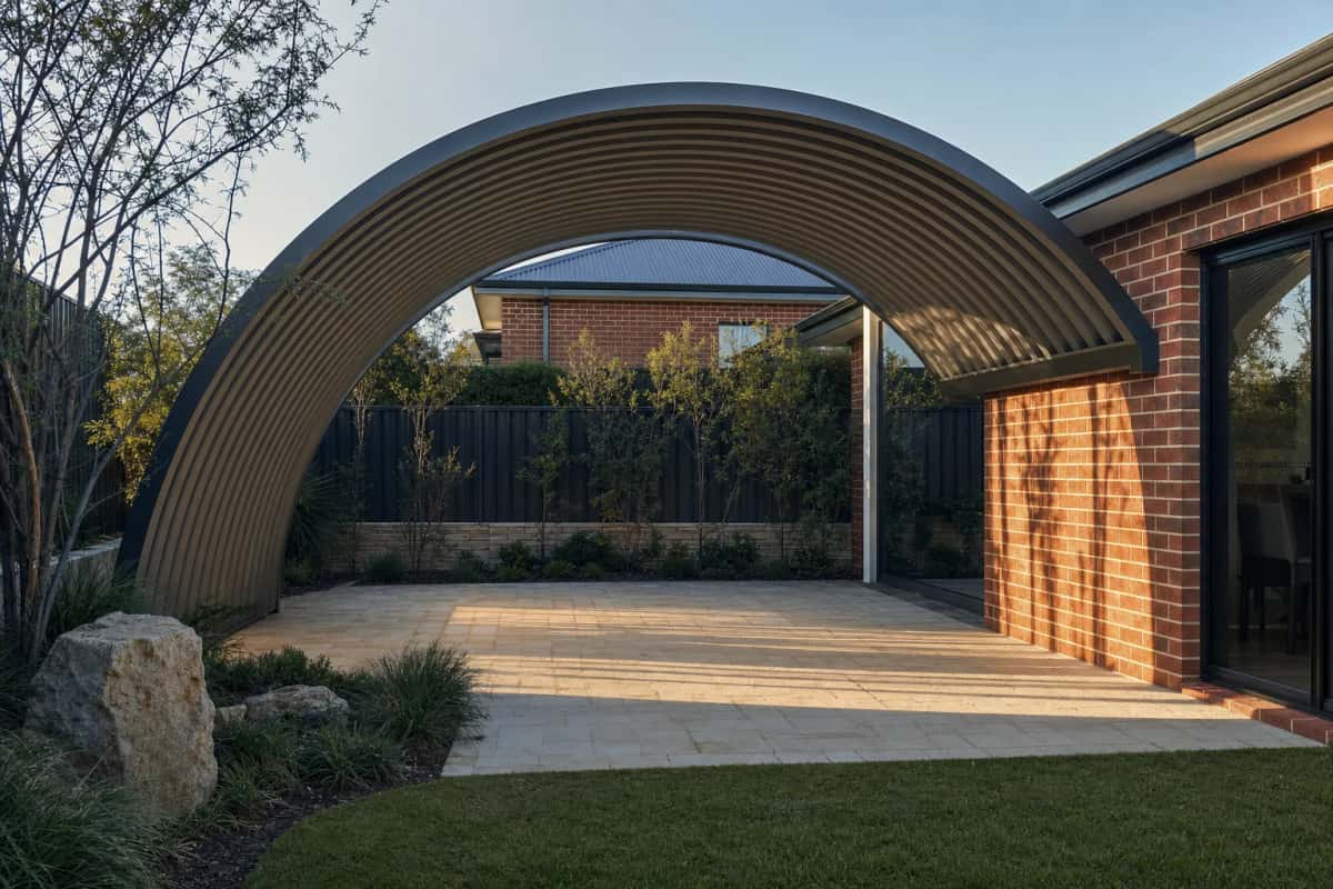 Curved dome patio roof spanning a paved area beside a brick home