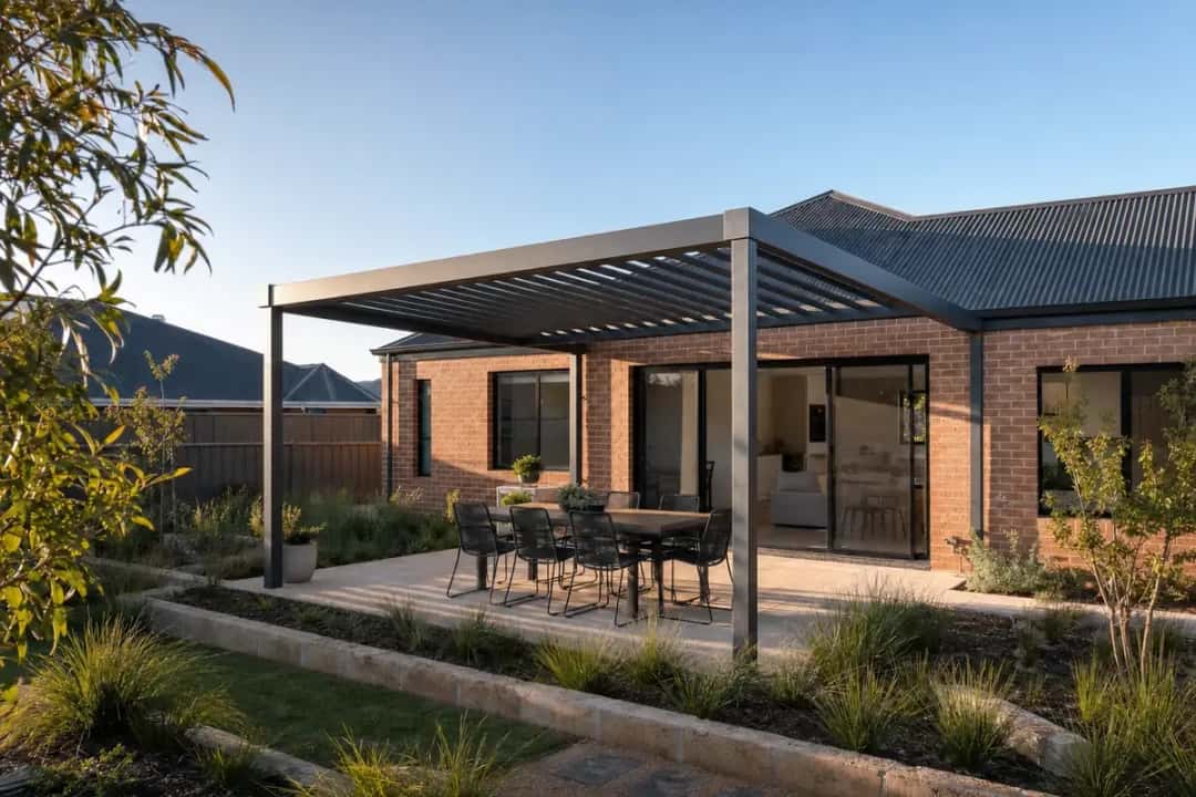Charcoal steel pergola with an open batten roof over limestone paving and an outdoor table