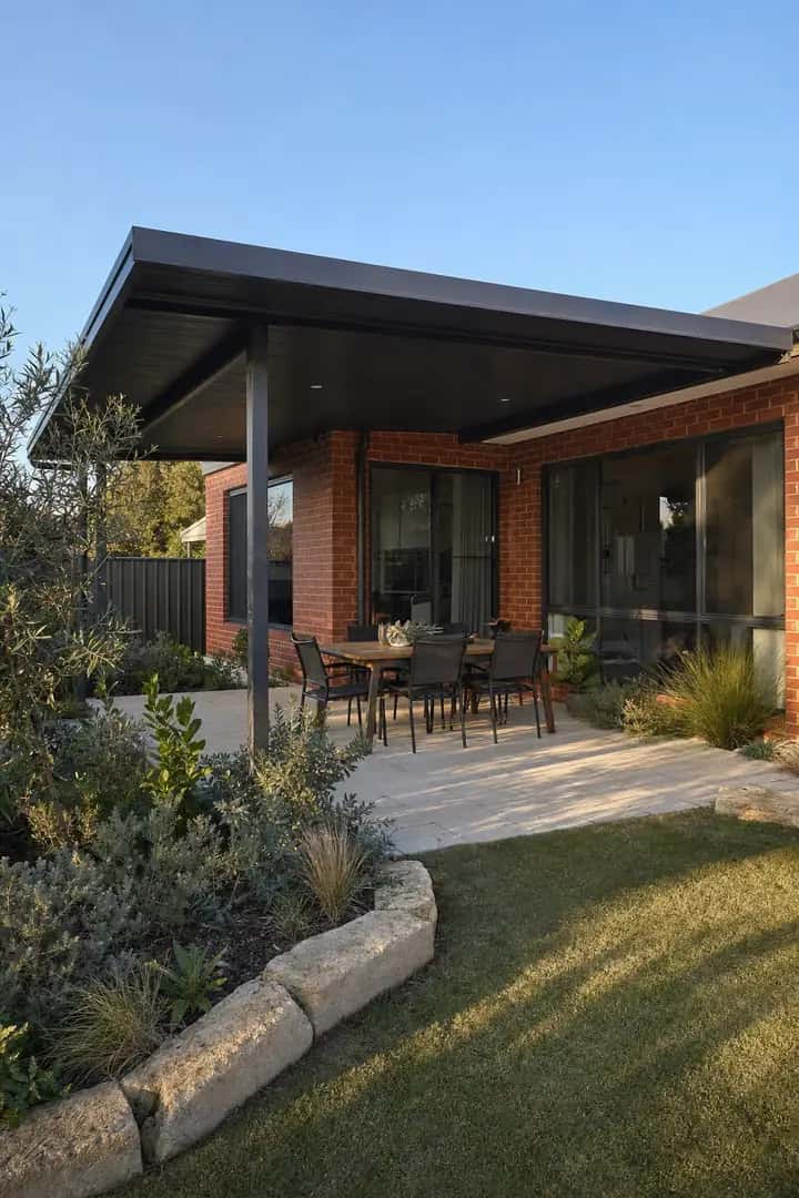 Charcoal skillion patio off a red brick home over a paved dining area, native garden and lawn in front